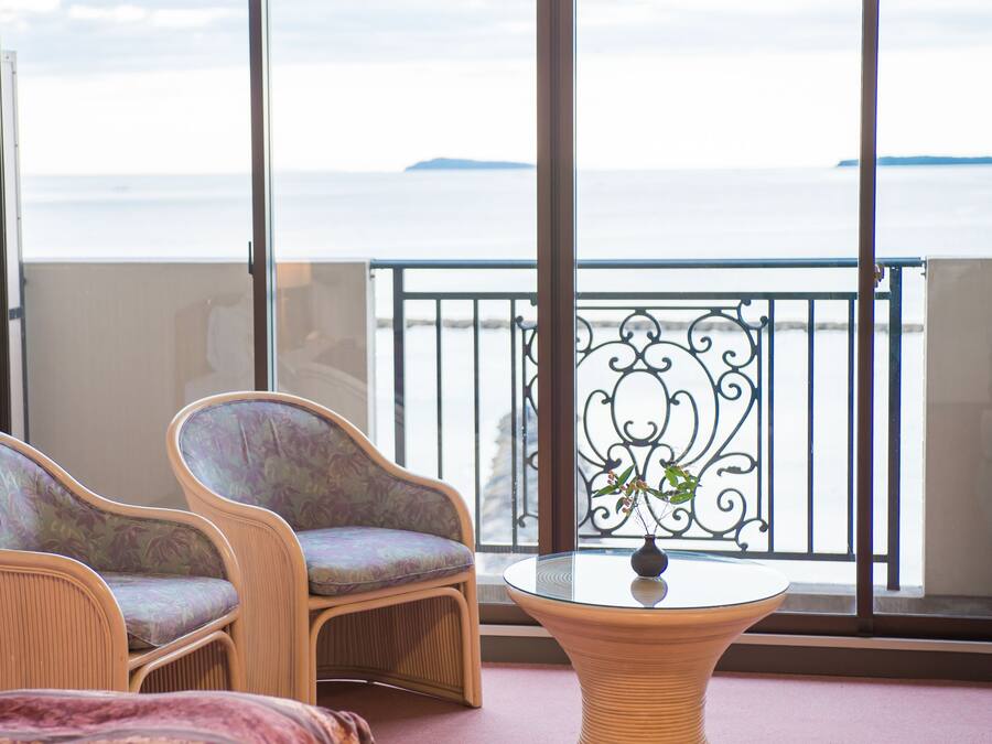 A balcony with two wicker chairs and a small table, overlooking a body of water.