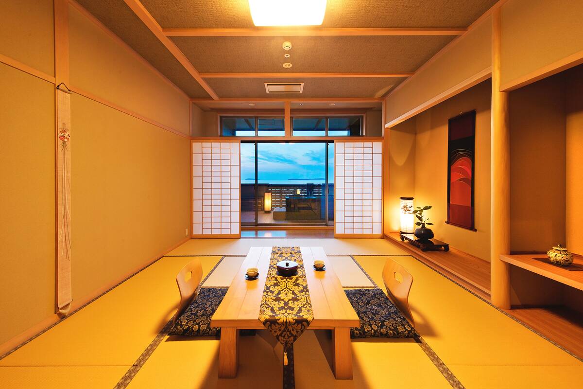 Ein traditioneller japanischer Raum mit Tatami-Böden, einem niedrigen Tisch mit dekorativer Tischläufer und Blick auf den Himmel durch Schiebetüren.
