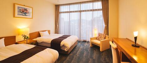 A hotel room with two beds, a desk, a chair, and a large window with curtains.