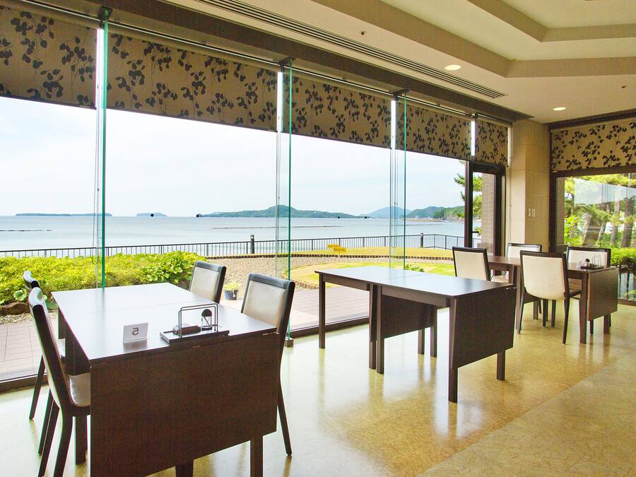 Un salón de conferencias con una gran mesa y sillas, ventanas amplias con vistas a una masa de agua y tierra distante, y una puerta que da a otra habitación.
