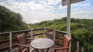 A wooden deck with a round table and two chairs, overlooking a coastal landscape with dense greenery and a clear sky. - Pine Lodge Resort (Gqeberha (Port Elizabeth))