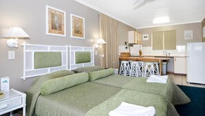 A hotel room with a bed, a desk, a kitchenette, and a ceiling fan. - Pine Lodge Resort (Gqeberha (Port Elizabeth))