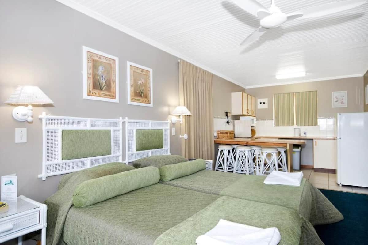 A hotel room with a bed, a desk, a kitchenette, and a ceiling fan.
