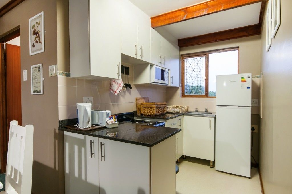 A compact kitchen with white cabinets, a microwave, a refrigerator, and a window with a view.