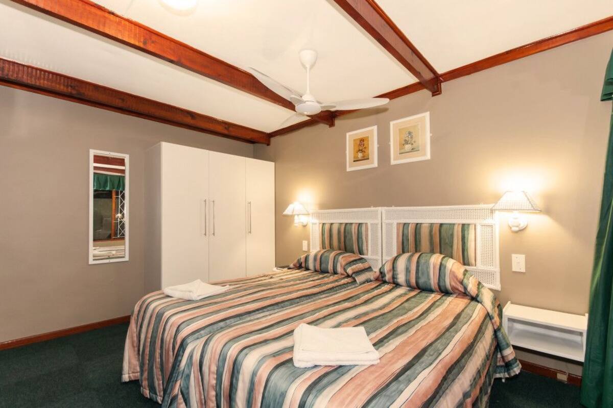 A hotel room with a large bed, a ceiling fan, a window with a curtain, and a wall-mounted light fixture.
