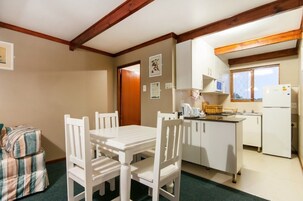 Una habitación pequeña y acogedora con una mesa y sillas blancas, una kitchenette con refrigerador y microondas, y una puerta que da a otra habitación.