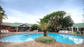 A swimming pool with a brick deck, surrounded by lounge chairs and palm trees. - Pine Lodge Resort (Gqeberha (Port Elizabeth))
