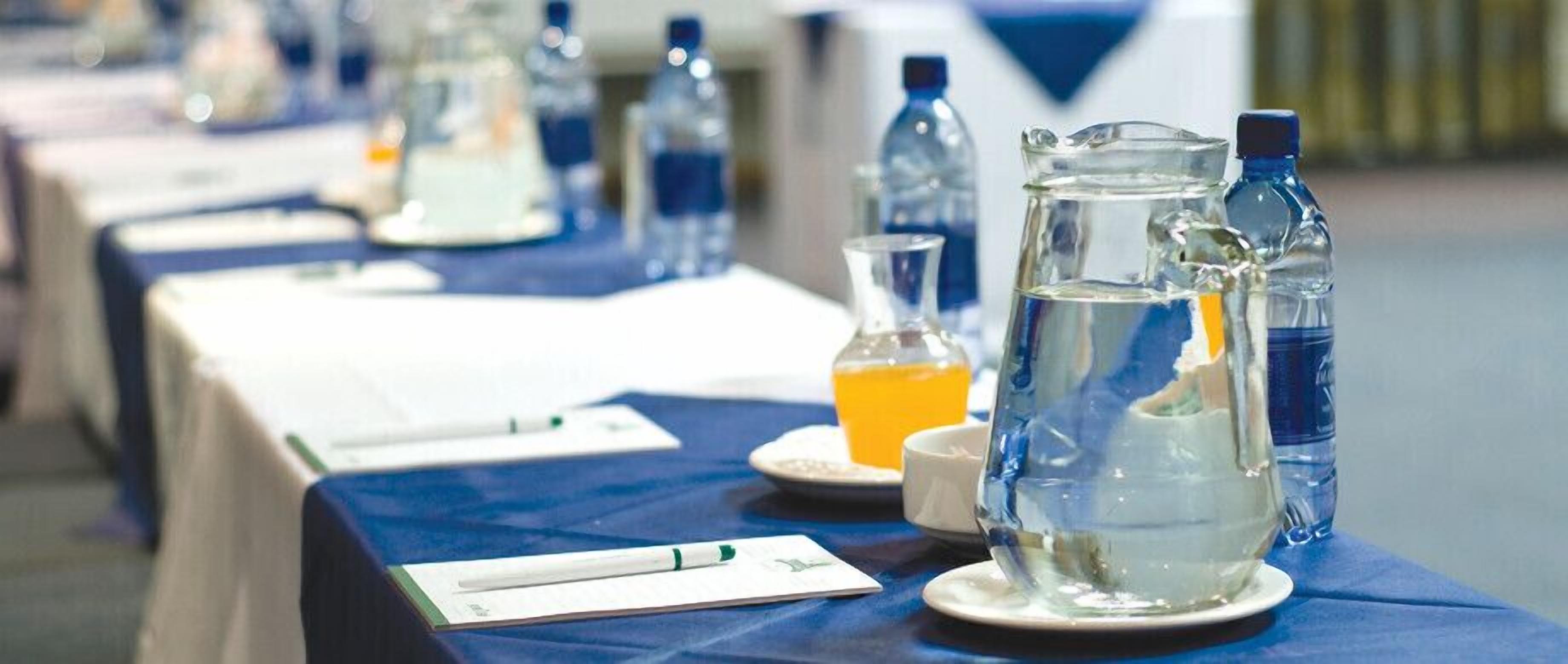 Una mesa con botellas de agua, una jarra de vidrio y un vaso de jugo de naranja.