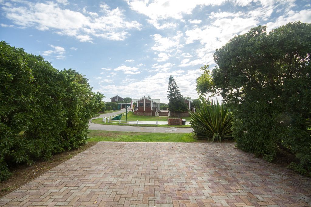 A paved pathway leading to a building with a brick facade, surrounded by well-maintained hedges and a large tree.