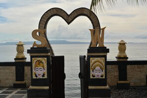 A heart-shaped archway with large letters 'S' and 'W' at a coastal entrance with decorative pillars and a view of the sea. - Segara Wangi Beach Cottages (Karangasem)