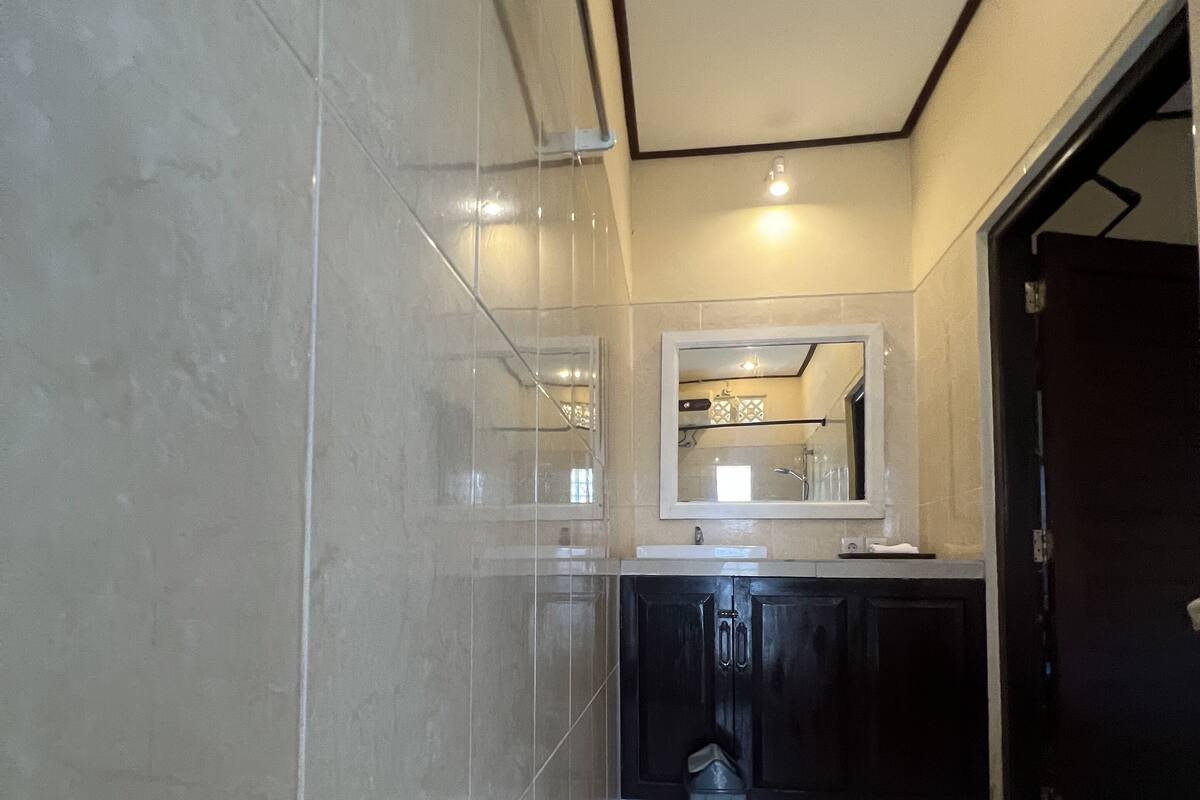 Un baño con inodoro, lavabo y espejo. Hay un cesto de basura al lado del lavabo. Las paredes y el suelo están cubiertos de azulejos.