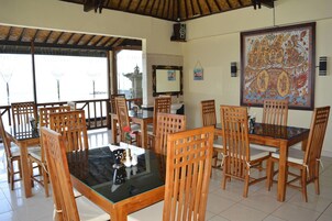 Un comedor con sillas de madera y una mesa de vidrio, un gran adorno en la pared, y vistas a través de un ventanal.