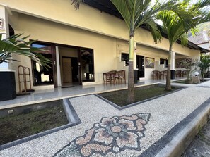 A hotel with a tiled patio, outdoor seating, and a palm tree. - Segara Wangi Beach Cottages (Karangasem)