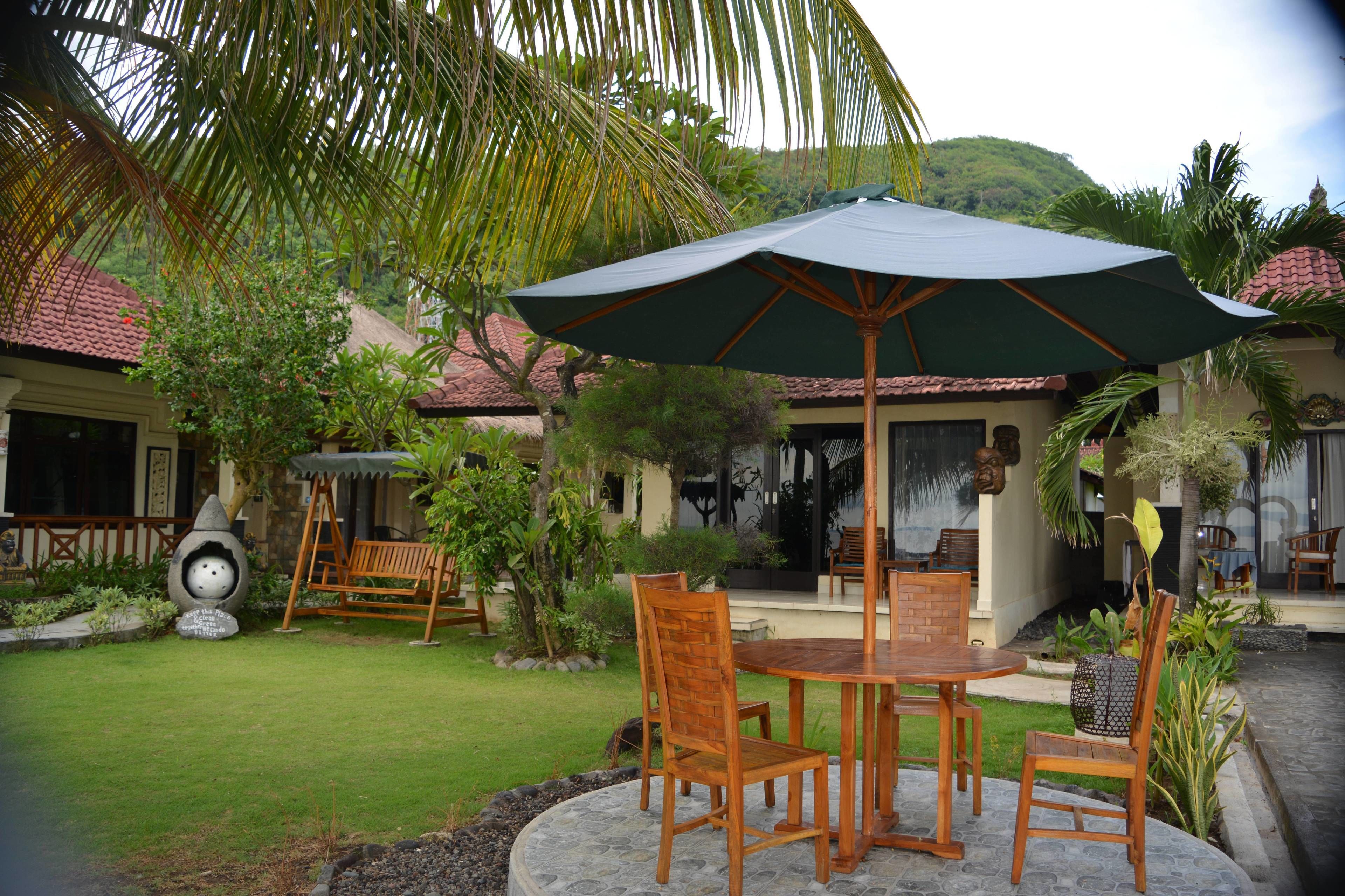 A patio with a table and chairs, surrounded by lush greenery and a large umbrella.
