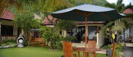 A patio with a table and chairs, surrounded by lush greenery and a large umbrella.
