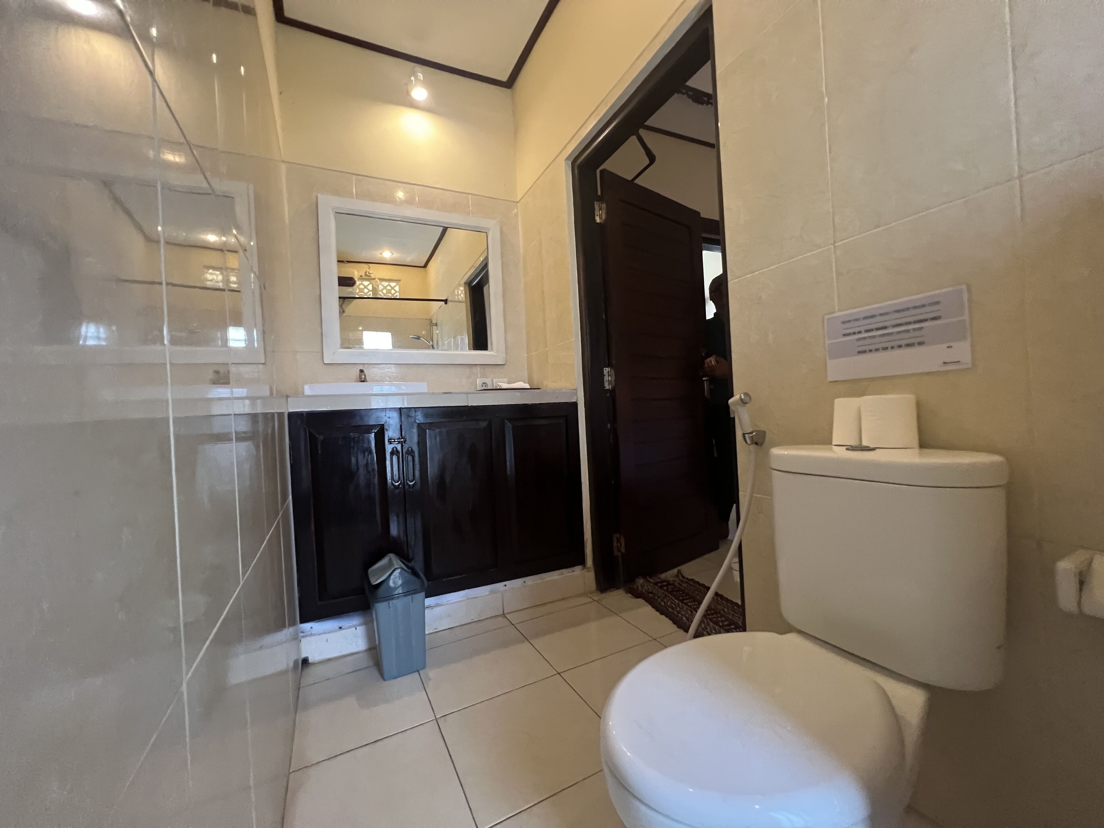 A bathroom with a white toilet, a sink with a mirror above it, and a trash bin.
