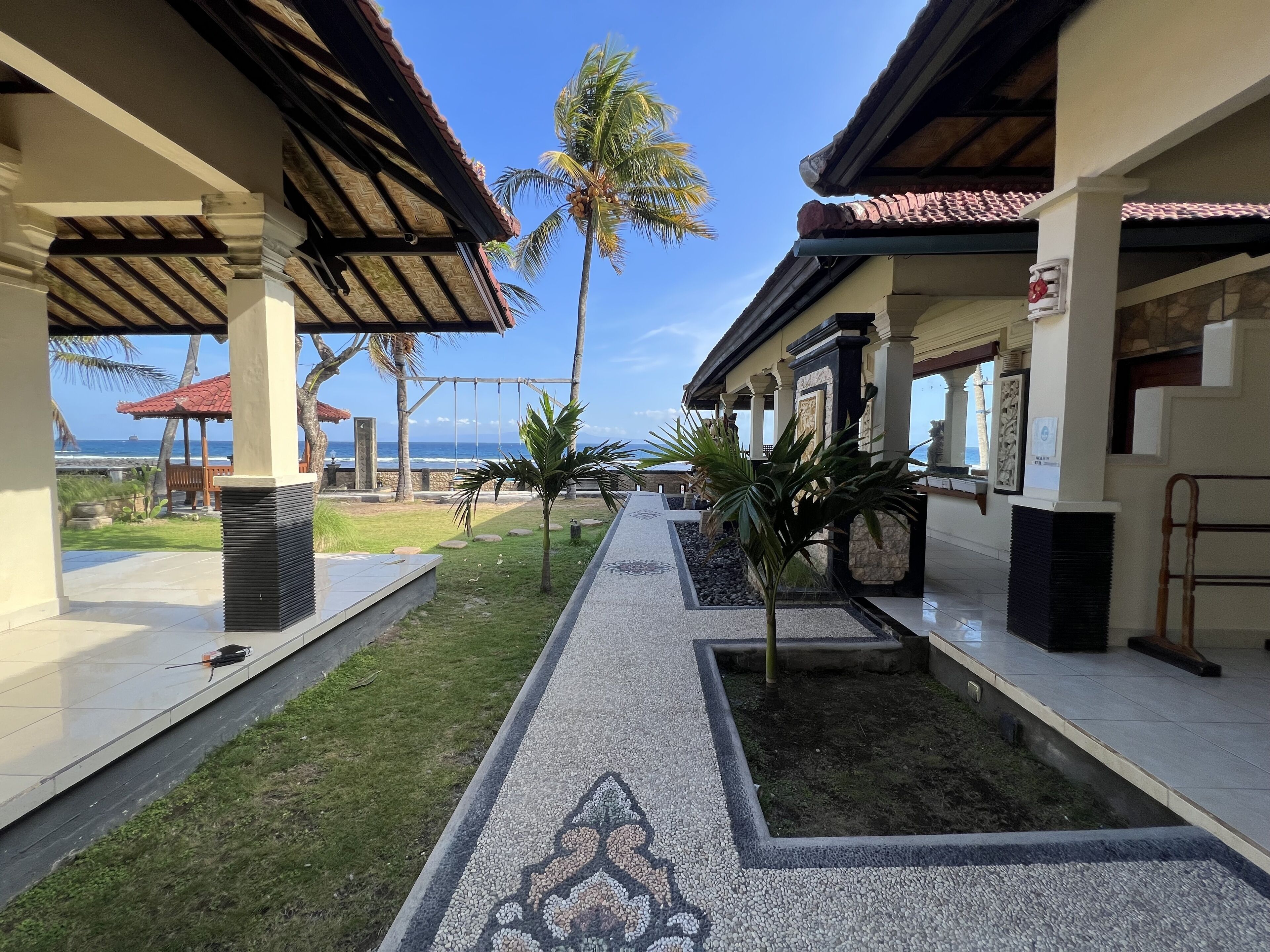 A covered walkway with a patterned floor leading to a building with columns and a tiled roof.