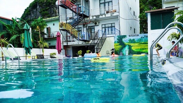 Ein Schwimmbad mit klarem Wasser, umgeben von Gebäuden mit Balkonen und einem Wandbild einer Landschaft.