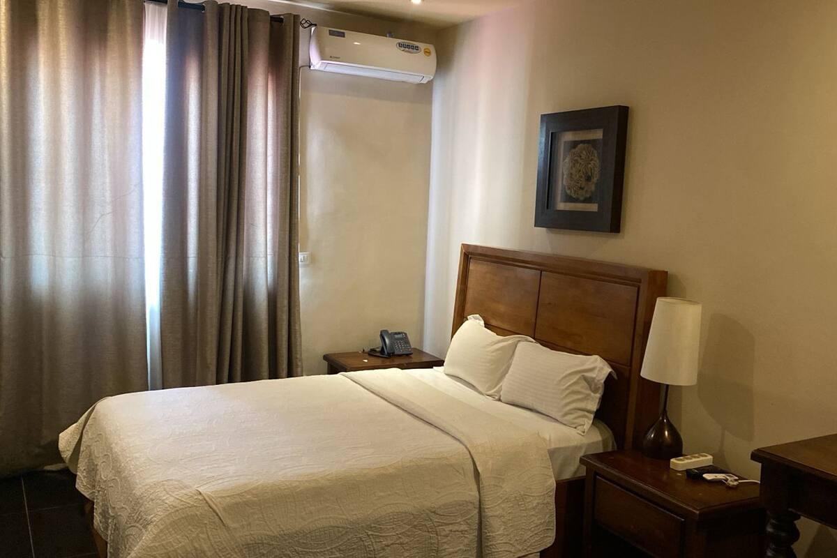 A hotel room with a bed, a bedside table with a lamp, a phone, and a picture on the wall.