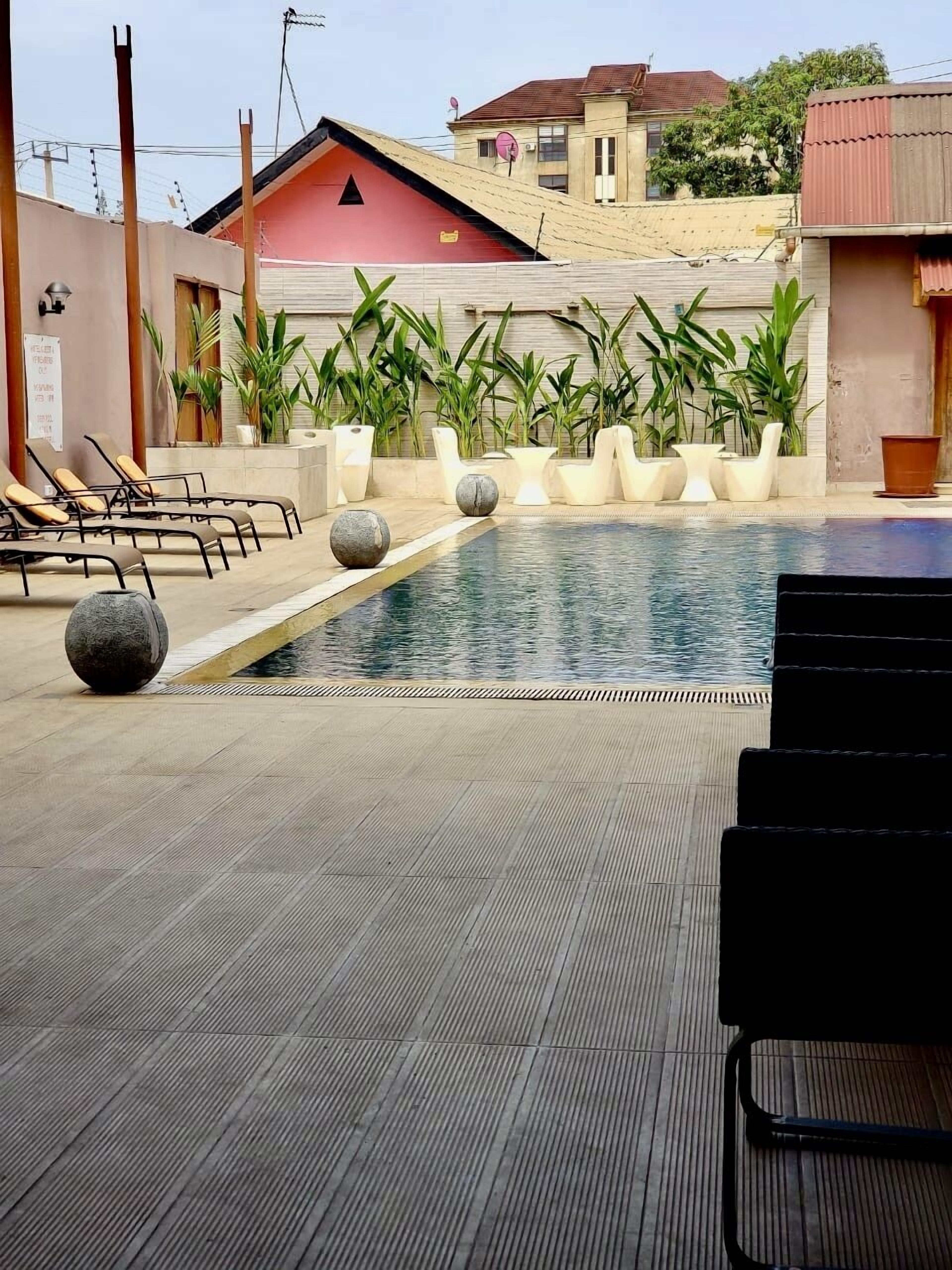 Zona de piscina con sillas de descanso, plantas en macetas y un suelo de baldosas.