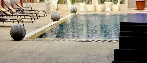 Zona de piscina con sillas de descanso, plantas en macetas y un suelo de baldosas.