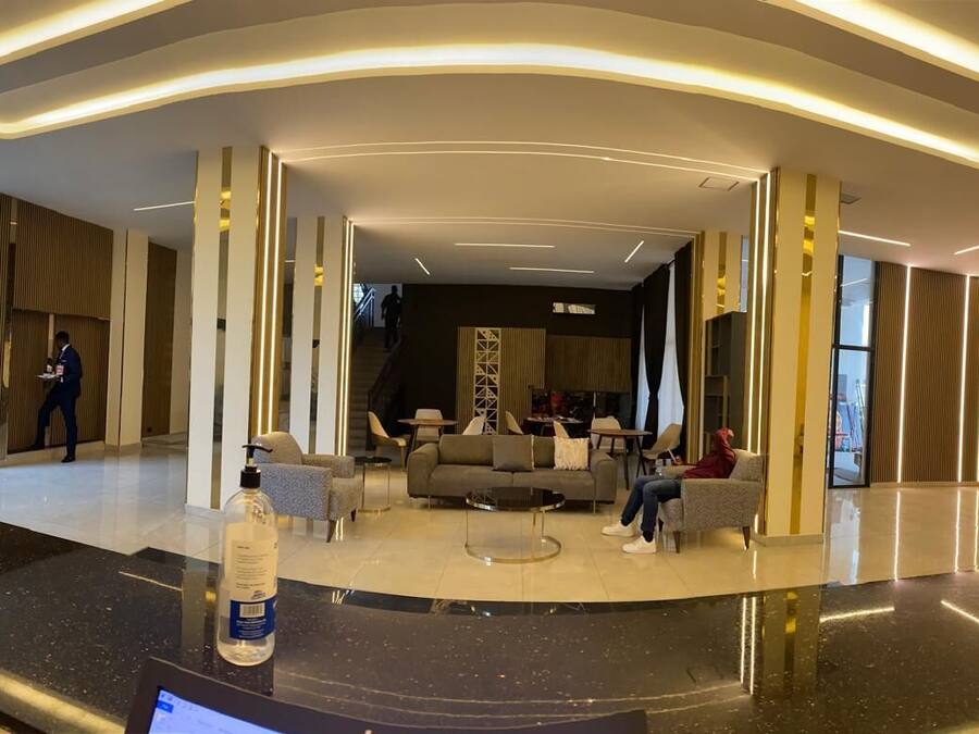 A modern lobby with a seating area, a reception desk, and a staircase leading to an upper floor.