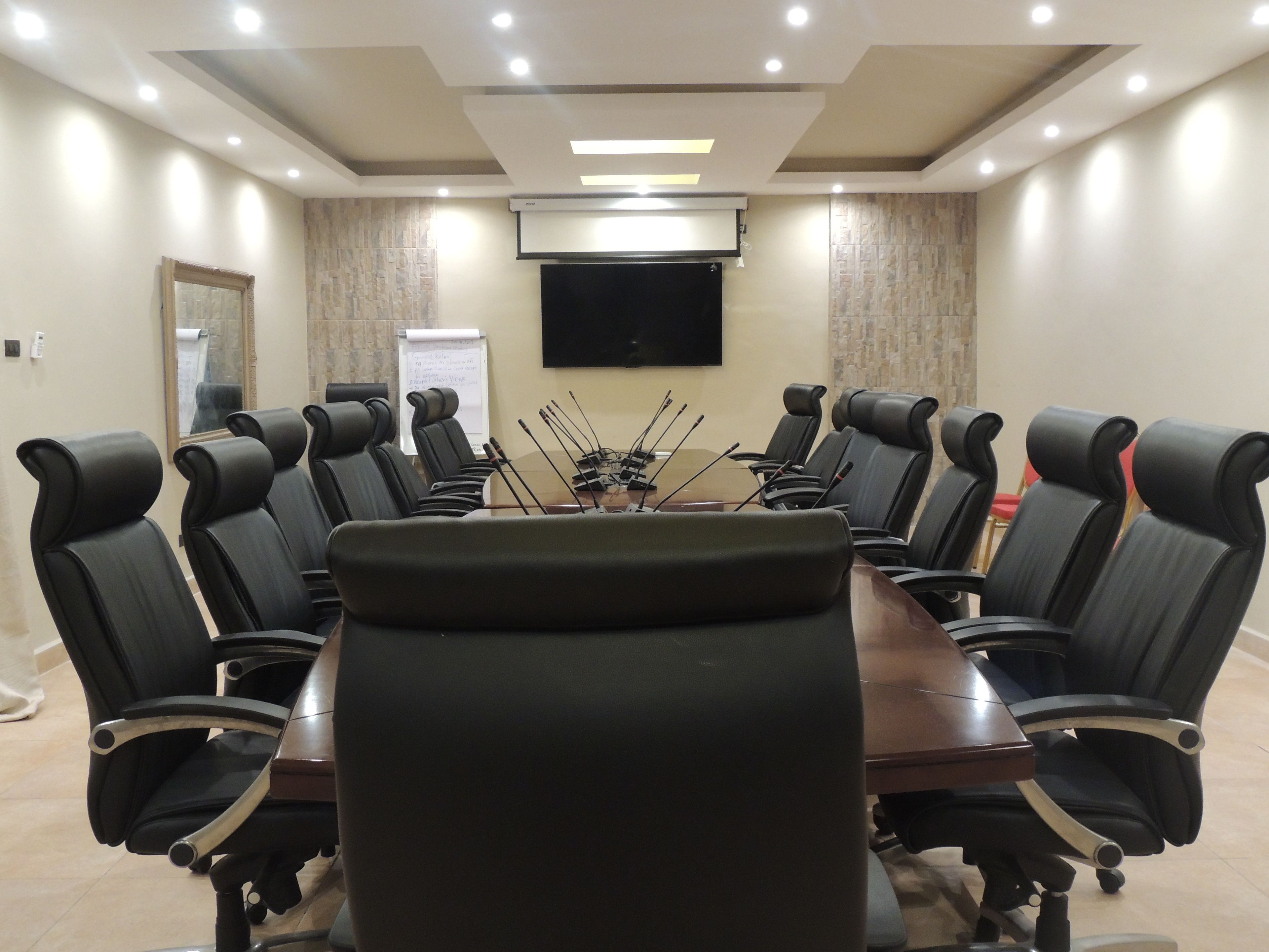 Una sala de conferencias con una mesa grande rodeada de sillas de cuero negro, un televisor de pantalla plana montado y una pizarra.