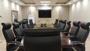 Una sala de conferencias con una mesa grande rodeada de sillas de cuero negro, un televisor de pantalla plana montado y una pizarra.