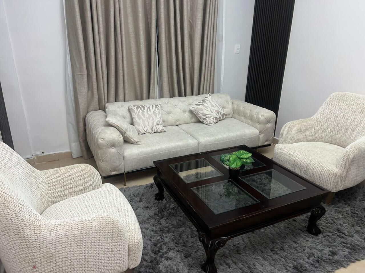 Un salon comprenant un canapé capitonné, deux fauteuils et une table basse avec un plateau en verre.