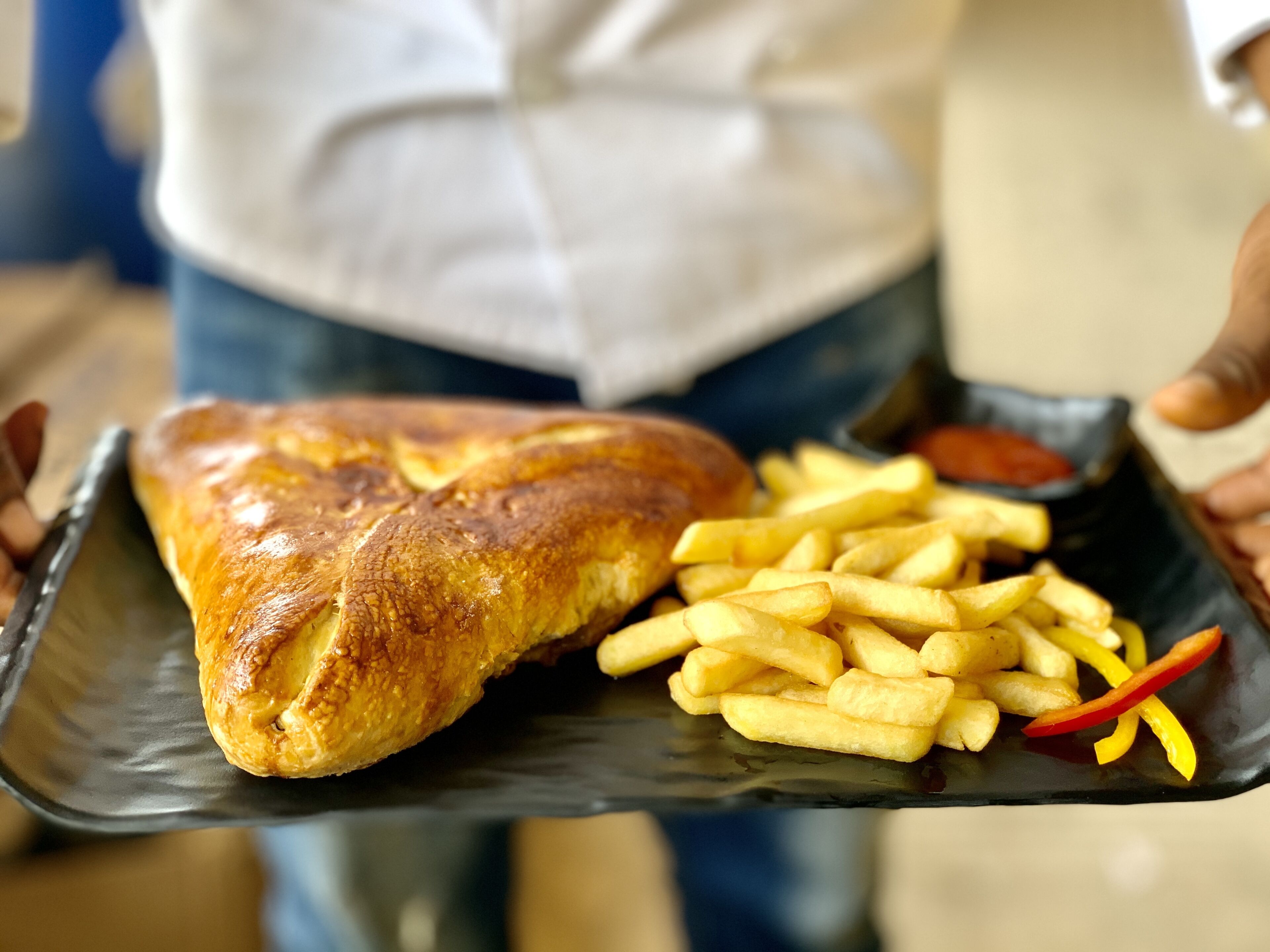 Una persona sostiene una bandeja negra con un croissant y papas fritas.