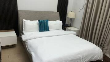 A hotel room with a bed, a nightstand, a lamp, and a curtain.