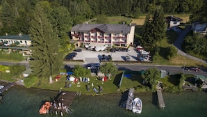 An aerial view of a hotel with a parking lot, a dock with boats, and a forested area in the background.