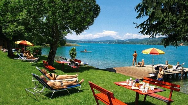 A lakeside setting with grassy areas, lounge chairs, and picnic tables.