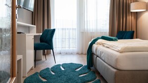 A hotel room with a bed, a desk with a chair, a TV, and a large window with curtains.
