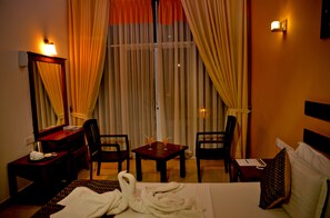 A hotel room with a bed, two chairs, a desk, a mirror, and a table with two drinks.