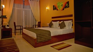 A hotel room with a large bed, a desk with a chair, a window with curtains, and artwork on the wall. - Peacock Heritage Anuradhapura (Anuradhapura)