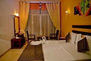 A hotel room with a bed, two chairs, a table with a lamp, and a painting on the wall. - Peacock Heritage Anuradhapura (Anuradhapura)