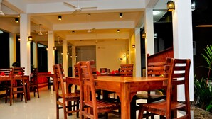 A spacious dining area with wooden tables and chairs, ceiling fans, and ambient lighting. - Peacock Heritage Anuradhapura (Anuradhapura)