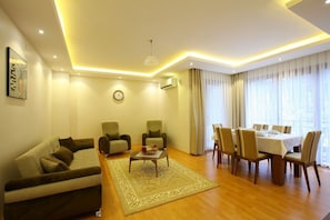 A modern living room with a sofa, chairs, a dining table set for six, and a large window with curtains. - Ugur Termal Residence (Termal)