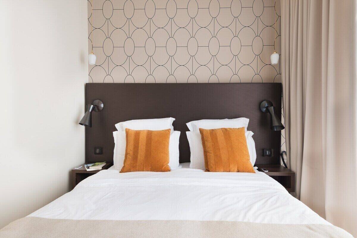 A neatly made bed with white and mustard pillows, a dark headboard, and two bedside lamps.