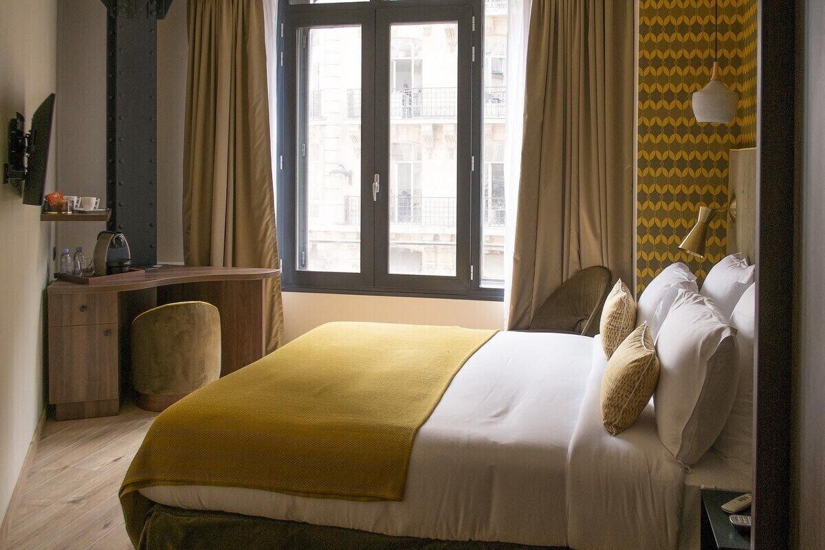 Habitació d'hotel amb llit, escriptori, cadira, finestra amb cortines i paret amb disseny.