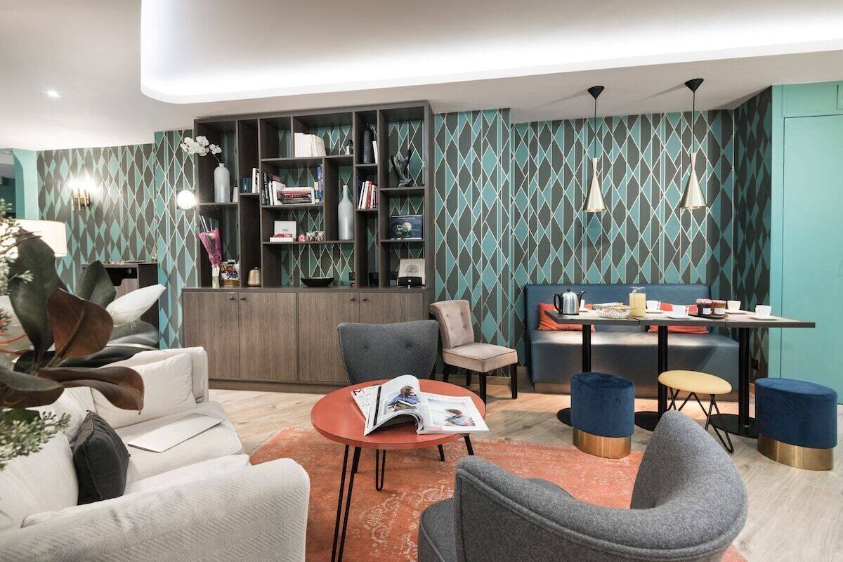 A modern living room with a sofa, armchairs, a coffee table, and a dining area with a table and chairs. There is a bookshelf filled with books and decorative items.