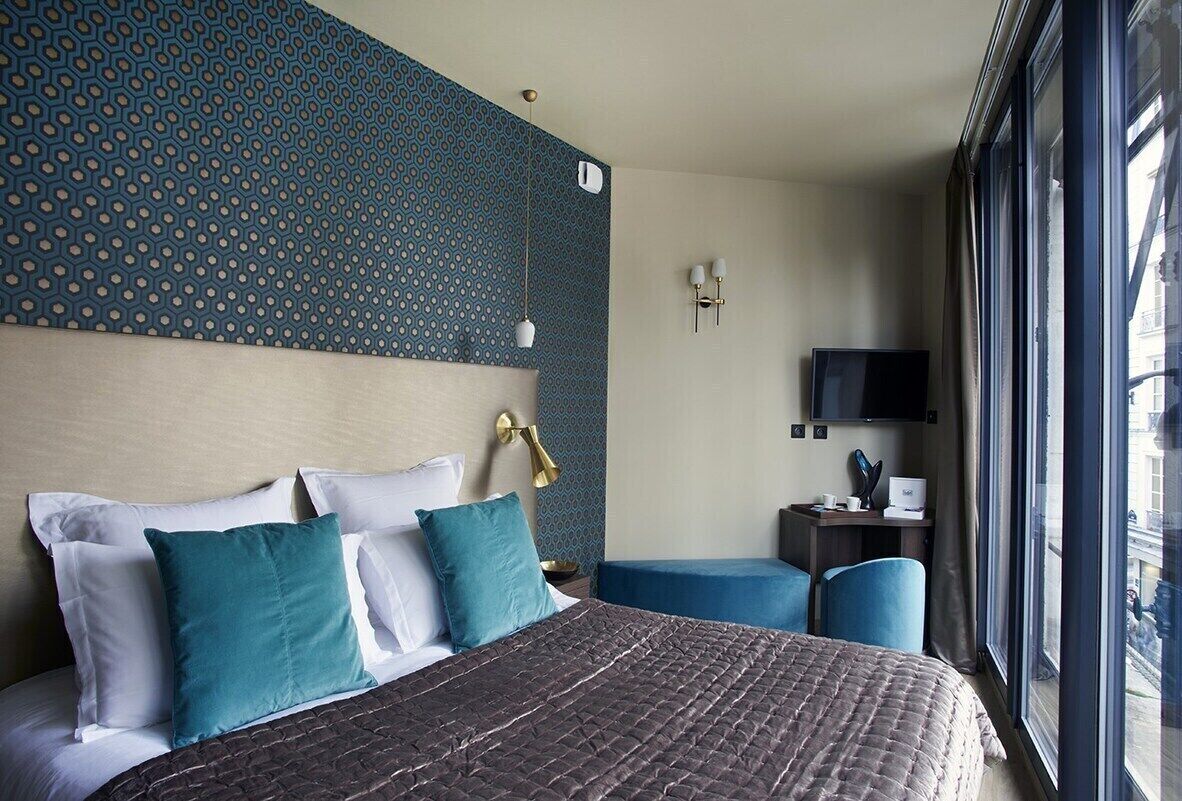 A hotel room with a large bed, a TV, and a window with a view of the city.