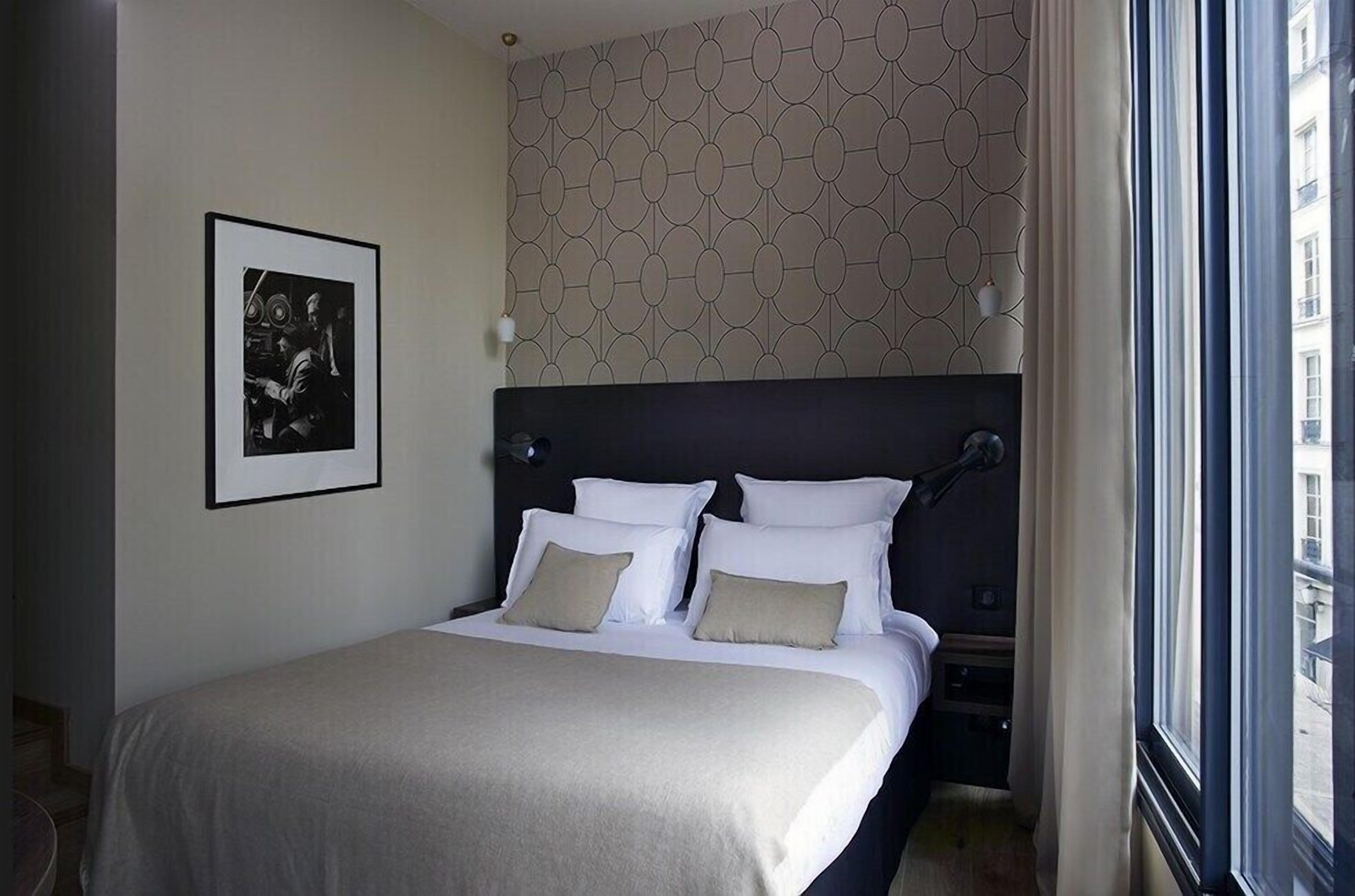 Habitación de hotel con una cama grande, cabecera, un cuadro enmarcado en la pared y una ventana con cortinas.