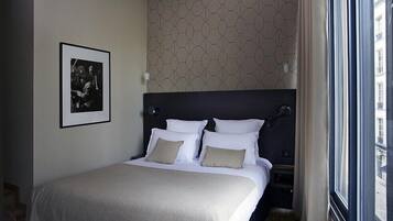 Habitación de hotel con una cama grande, cabecera, un cuadro enmarcado en la pared y una ventana con cortinas.