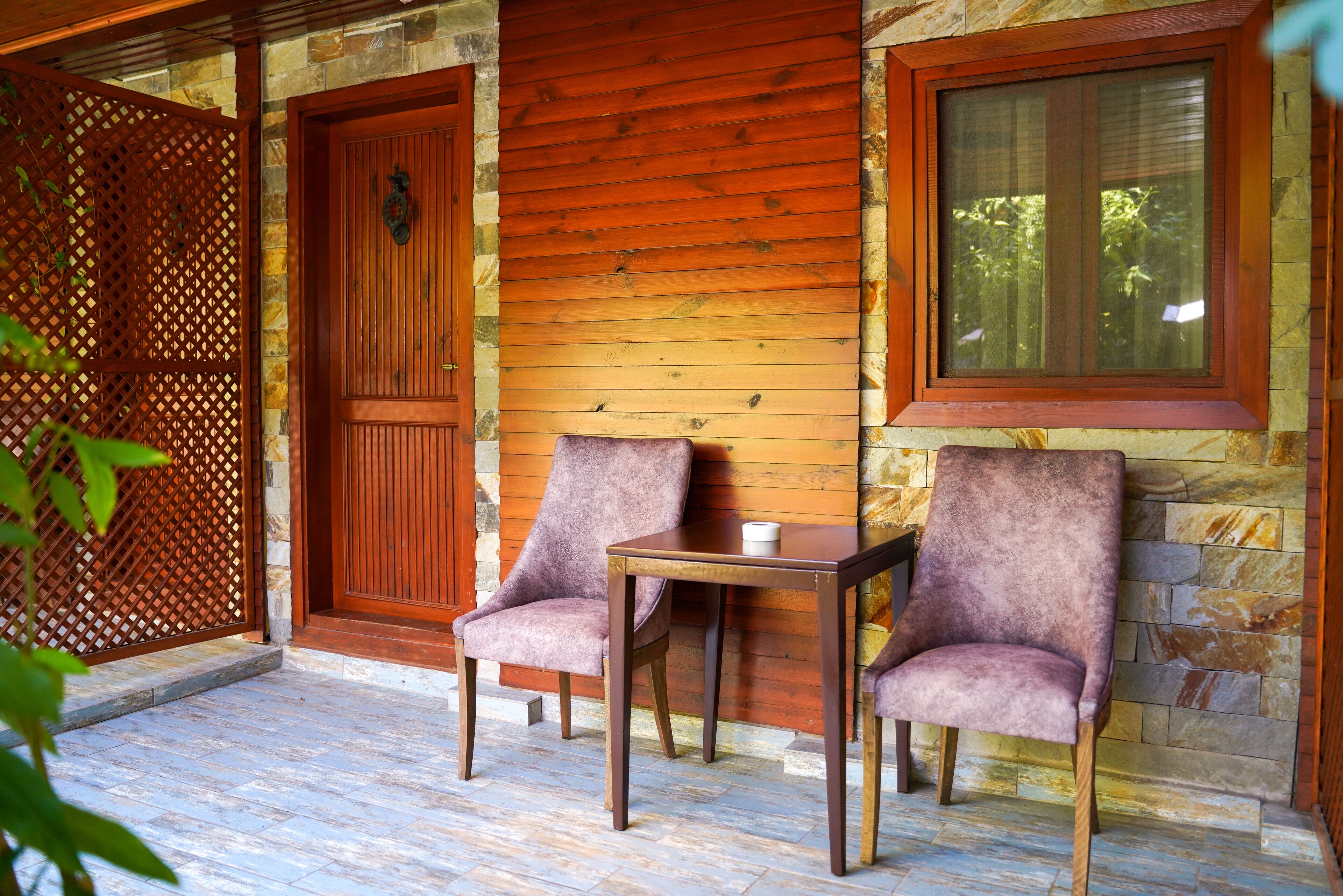 Un porche de pared de piedra con una puerta de madera, una ventana, dos sillas y una mesa.