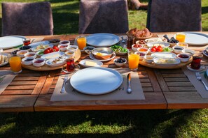 Une table en bois dressée pour le petit-déjeuner, avec des œufs, des toasts, des fruits et des boissons.