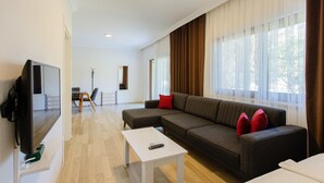 A modern living room with a sectional sofa, a flat-screen TV, a coffee table, and large windows with curtains.