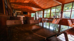 A wooden interior with a large dining table and chairs, large windows, and a rustic decor.