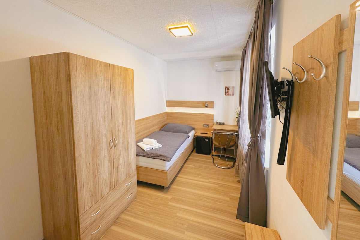 Une chambre à coucher de taille modeste, comprenant une armoire en bois, un lit simple, un bureau et une chaise.
